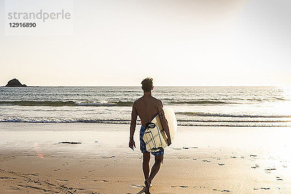 Young man walking on the beach  carrying his surfboard
