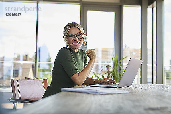 Portrait of smiling mature woman using laptop on table at home