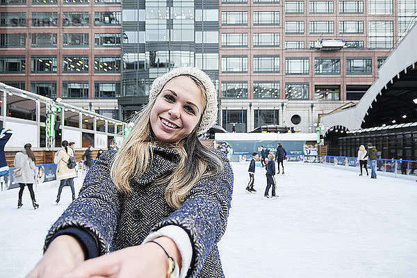 Blond young woman having fun ice skating  holding hands of young man