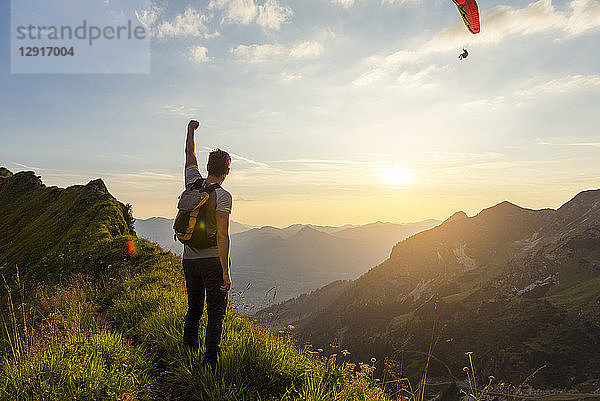 Germany  Bavaria  Oberstdorf  man on a hike in the mountains at sunset with paraglider in background