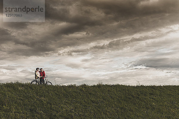 Senior couple with bicycles in rural landscape under cloudy sky