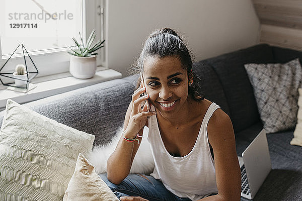 Portrait of smiling young woman on the phone sitting on the couch at home