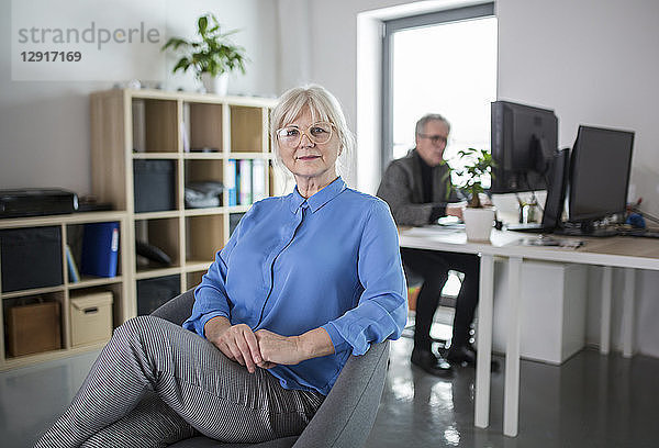 Senior businesswoman sitting in office with colleague working behind her