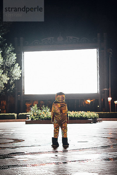 Spaceman on a square at night attracted by shining projection screen