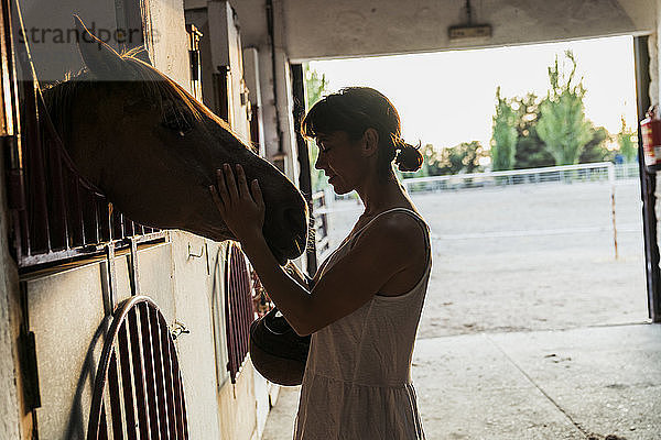 Woman stroking horse in stable