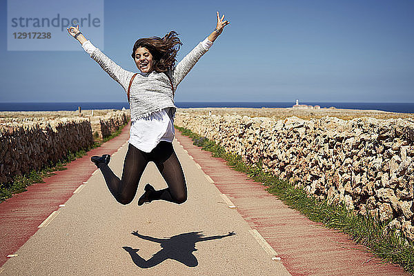 Cheerful young woman jumping in air with rising hands  outdoors