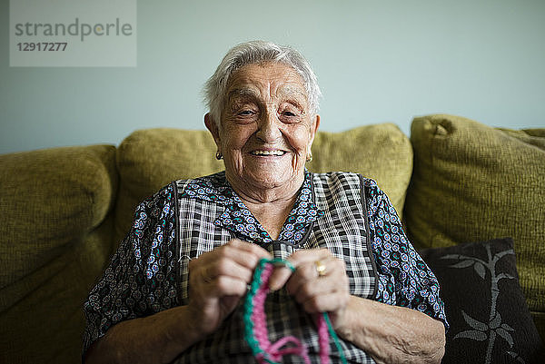 Portrait of smiling senior woman crocheting on the couch at home