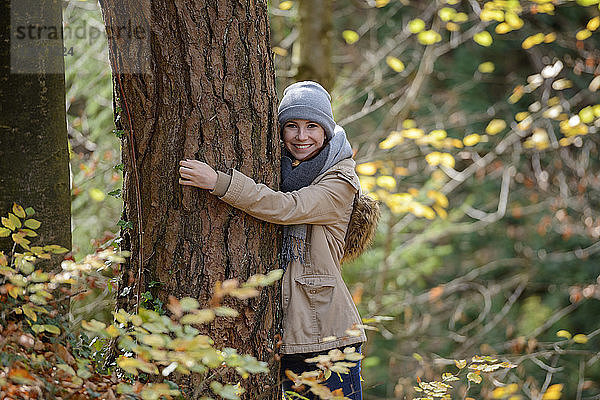 Portrait of smiling teenage girl hugging tree trunk in autumnal forest