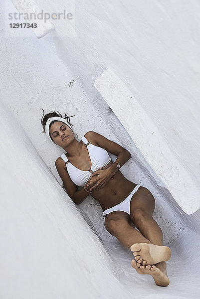 Young woman wearing white bikini lying in a wall niche  top view