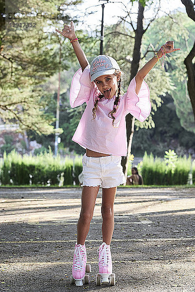Happy little girl raising arms while roller skating in a park