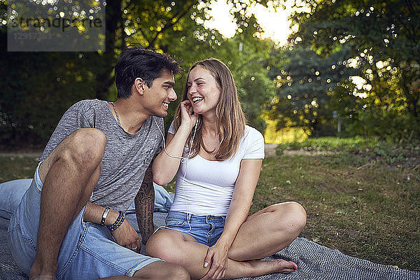 Young couple sitting in park  sharing earphones  listening music