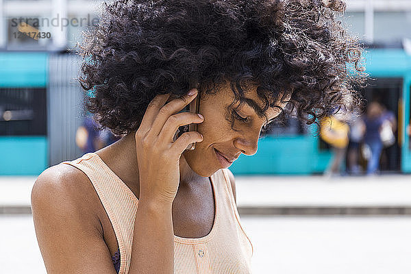 Germany  Frankfurt  portrait of smiling young woman with curly hair on the phone