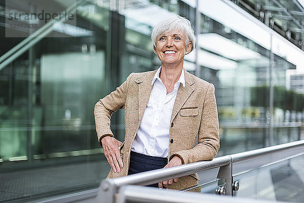 Portrait of smiling senior businesswoman leaning on railing in the city