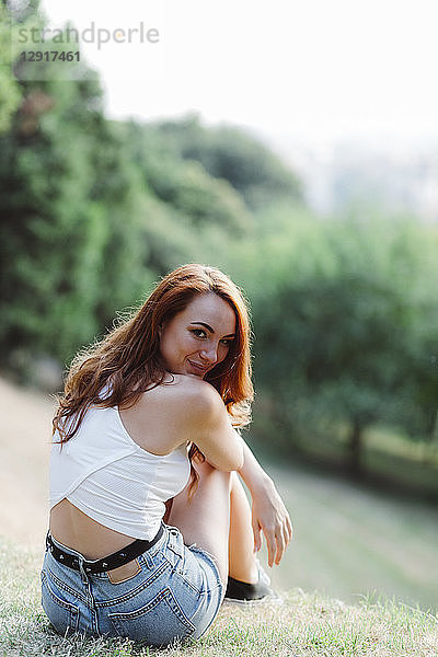 Smiling redheaded woman relaxing on hill in a park