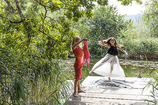 Two girls on jetty at a pond in fancy dresses