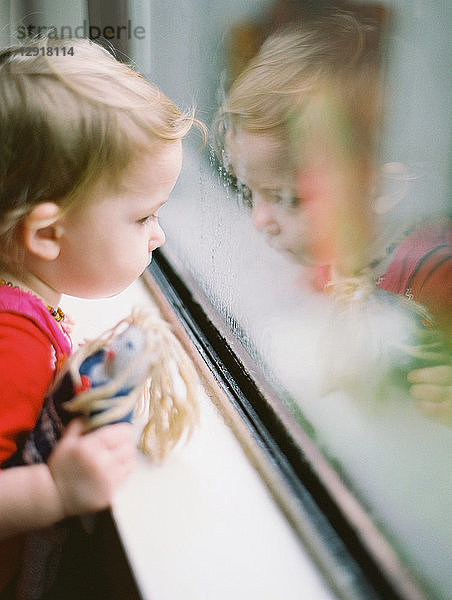 Kleines Mädchen hält Puppe und schaut durch ein Fenster  Vancouver  British Columbia  Kanada