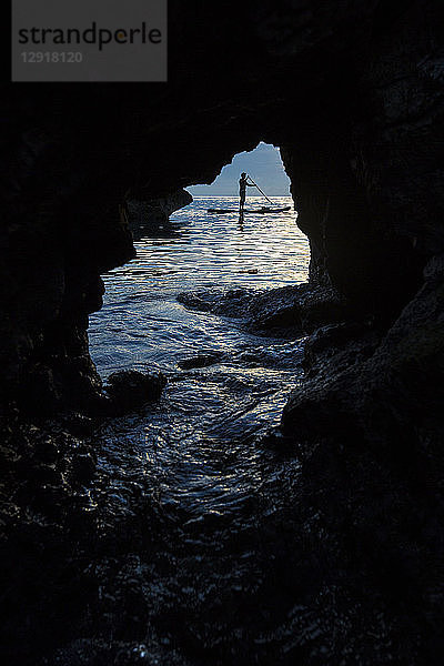 Blick aus einer Höhle auf die Silhouette eines Mannes  der im Meer paddelt  Misool  Raja Ampat  Indonesien