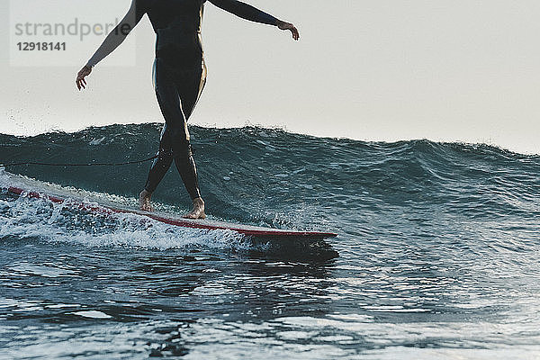 Tiefschnitt eines Surfers im Neoprenanzug beim Surfen auf dem Longboard
