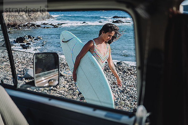 Blick aus dem Inneren eines Wohnmobils auf eine Surferin  die mit ihrem Surfbrett am Strand spazieren geht  Teneriffa  Kanarische Inseln  Spanien