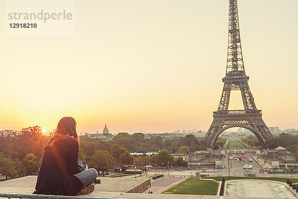 Junge Frau sitzt und betrachtet den Eiffelturm bei Sonnenuntergang  Paris  Ile-de-France  Frankreich