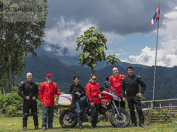 Gruppe von Freunden  die zusammen neben einem Motorrad posieren  mit einem bewaldeten Hügel im Hintergrund  Nan ¬ÝMueang¬ÝChiang¬ÝRai¬ÝDistrikt  Thailand