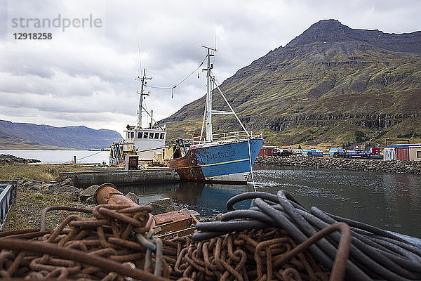 Rostige Ketten vor einem alten  verlassenen Fischerboot  das im Hafen einer kleinen Küstenstadt vertäut ist  Seydisfjordur  Island