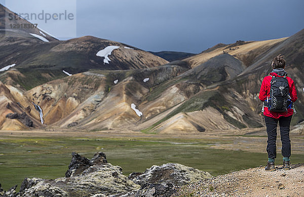 Wanderer bewundert die Landschaft mit Rhyolithbergen bei Landmannalaugar auf dem Laugarvegur-Wanderweg bei Tageslicht  Landmannalaugar  Fjallabak  Island