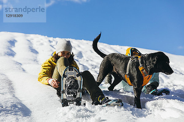 Hund wartet auf Besitzer  die im Schnee sitzen und Schneeschuhe anziehen  Whistler  British Columbia  Kanada