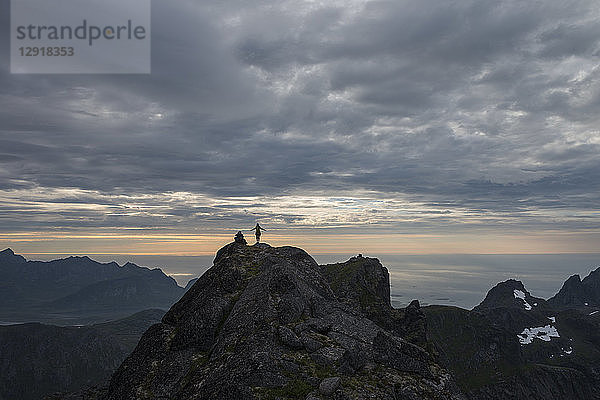 Fernsicht auf eine Wanderin auf dem Gipfel des Stjerntind bei Sonnenuntergang  höchster Gipfel der Gemeinde Flakstad  Flakstadoya  Lofoten  Norwegen