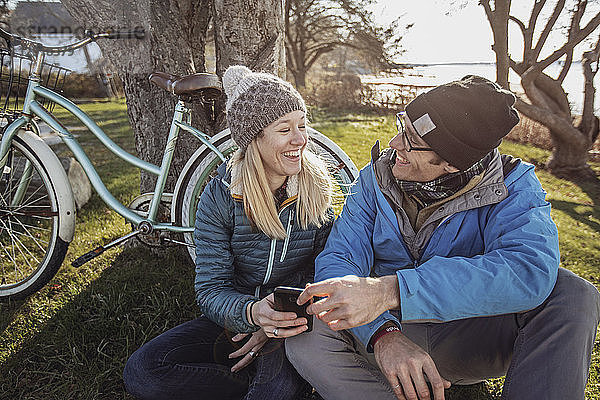 Junges Paar sitzt im Gras und benutzt sein Smartphone während einer Fahrradpause  Portland  Maine  USA