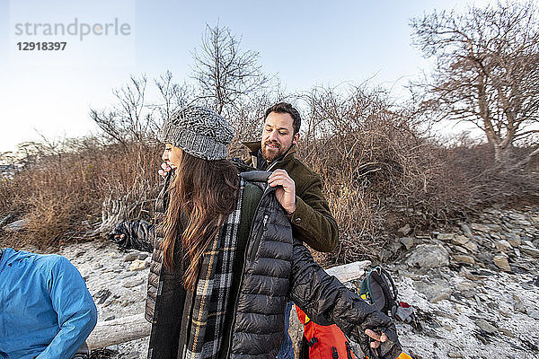 Mann hilft einer Freundin beim Anziehen der Jacke beim Zelten am Küstenstrand im Herbst  Portland  Maine  USA