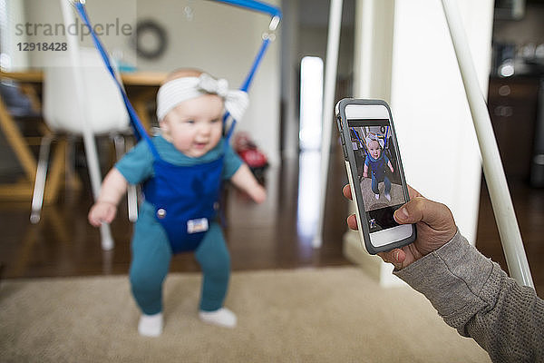 Eltern fotografieren ihr Baby in der Babywippe mit dem Smartphone zu Hause