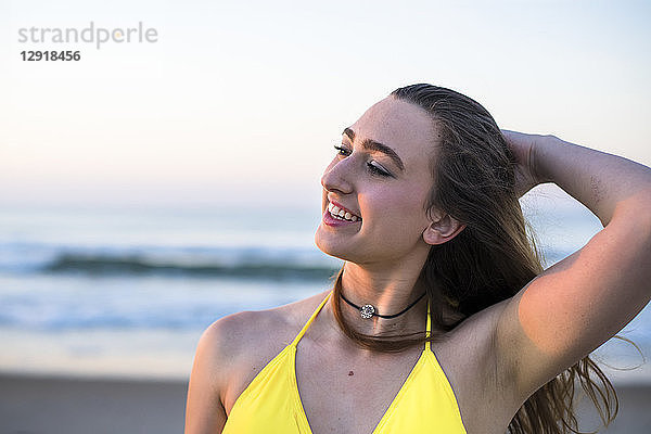 Kopf- und Schulteraufnahme einer lächelnden Frau im gelben Bikini am Strand mit der Hand im Haar