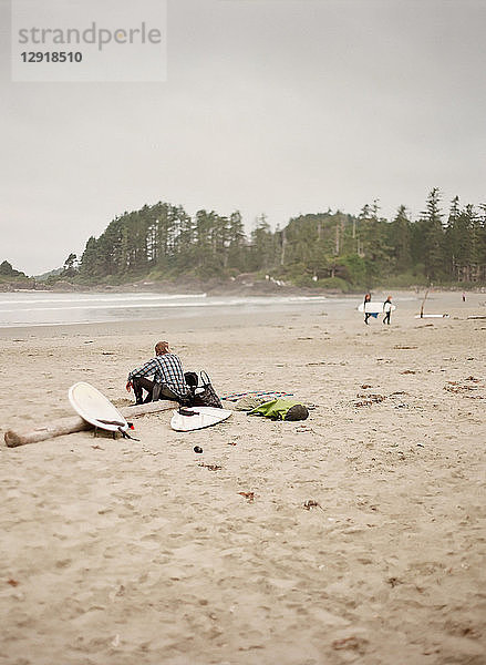 Surfer sitzt auf einem Baumstamm am Sandstrand  Vancouver  British Columbia  Kanada