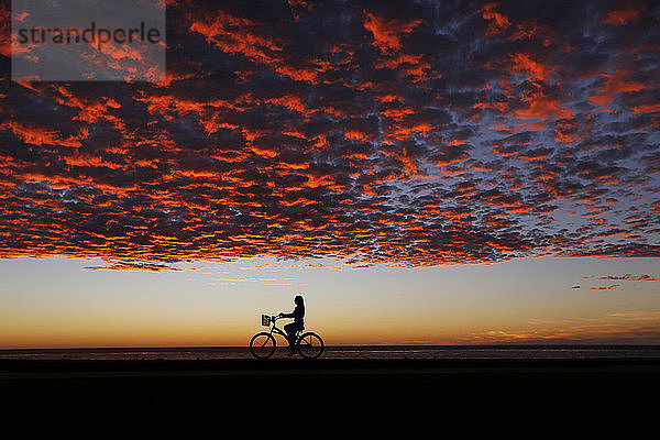 Einsame Frau reitet Silhouette Horizont unter launischen Sonnenuntergang Himmel  La Jolla  San Diego  Kalifornien  USA