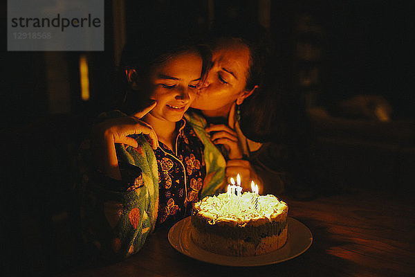 Mutter küsst Tochter zum Geburtstag vor Geburtstagskuchen auf dem Tisch