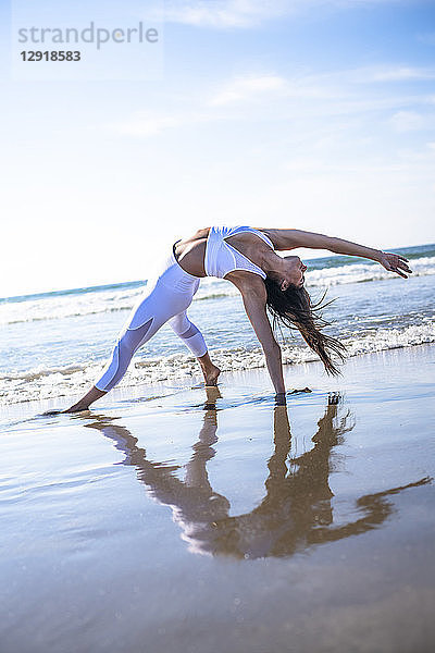 Ganzkörperaufnahme einer jungen Frau mit schwarzen Haaren beim Yoga am Strand