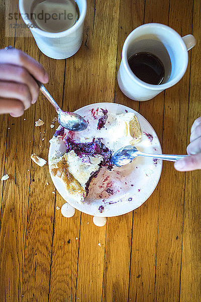 Zwei Hände greifen mit Gabeln in einen Teller mit Kuchen und Eiscreme  daneben stehen zwei Becher Kaffee.