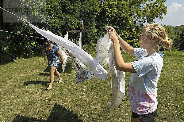 Eine Frau und ein Mädchen im Teenageralter hängen Wäsche zum Trocknen auf eine Wäscheleine im Freien