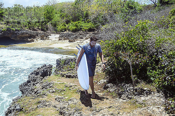 Vorderansicht eines Mannes  der ein Surfbrett am Strand trägt