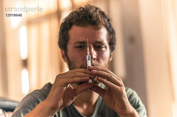 Blick auf einen einzelnen jungen Mann  der eine Spritze mit Impfstoff hält