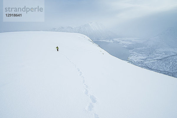 Fernblick auf einen Wanderer  der im Winter den Gipfel des Matmora-Gebirges besteigt  Austvagoy  Lofoten  Norwegen