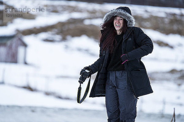 Dreiviertellängenaufnahme einer lachenden Frau mit Kamera im Winter  Tromso  Provinz Troms  Norwegen