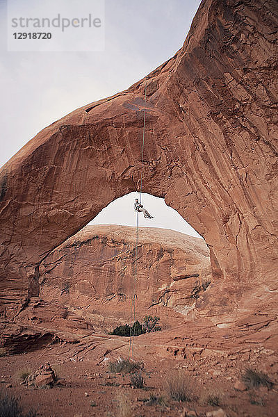 Kletterer  der unter einem erodierten natürlichen Bogen hängt  Moab  Utah  USA