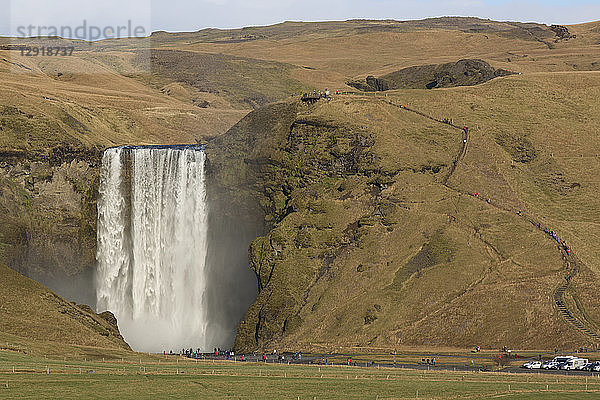 Eine große Gruppe von Touristen steht am Fuße des plätschernden Skogafoss-Wasserfalls  Island