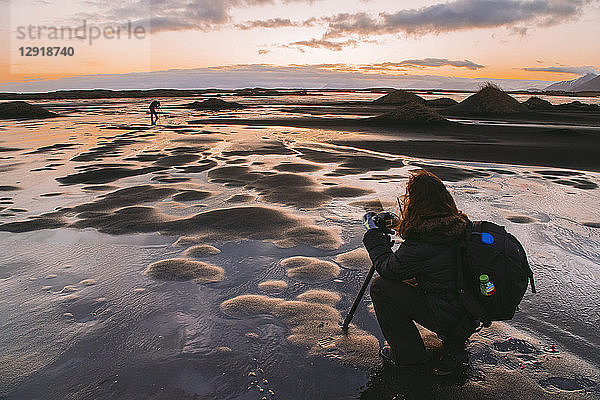 Weibliche Fotografin hockt bei der Aufnahme eines Fotos bei Sonnenuntergang  Island