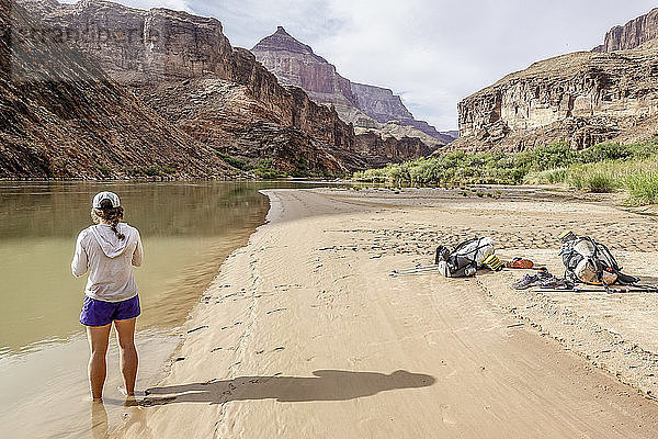 Junge Frau kühlt sich nach einem heißen Wandertag im Grand Canyon ab  indem sie ihre Füße in den Colorado River taucht  Grand Canyon  Arizona  USA