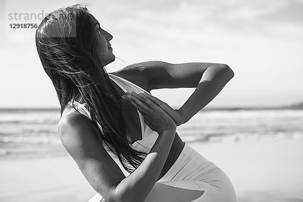 Foto einer jungen Frau  die am Strand mit verschränkten Händen Yoga macht
