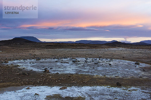 Blau gefärbte Mineralien  die von vulkanischen Schlammpfützen und Dämpfen zurückgelassen werden  kontrastieren mit dem orangefarbenen Himmel im geothermischen Gebiet Hverarˆšˆ'ndor Hverir am Namaskard-Pass in Nordisland.