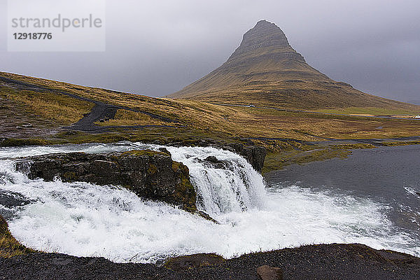 Blick auf den plätschernden Wasserfall Kirkjufellsfoss und den Berg Kirkjufell an einem grauen Tag  Island